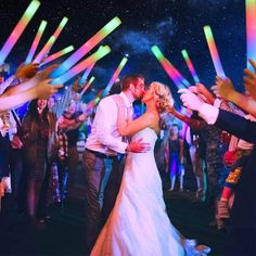 a bride and groom kissing in front of their wedding party with colorful lights on the dance floor