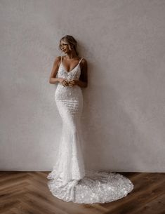 a woman standing in front of a white wall wearing a wedding dress with spaghetti straps