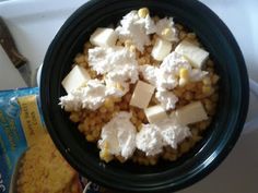 a black bowl filled with corn and cheese on top of a white counter next to a bag of chips