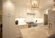 a large kitchen with white cabinets and marble counter tops, gold chandelier above the stove