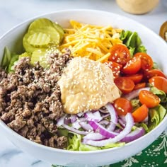 a white bowl filled with meat, vegetables and dressing on top of a green napkin