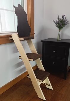 a black cat sitting on top of a wooden step ladder next to a dresser and window