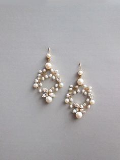 two pairs of pearl and crystal earrings on top of a gray surface with white beads