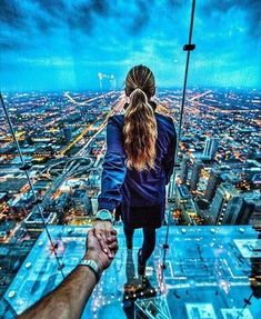 a man and woman holding hands while standing on top of a skyscraper