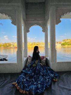 a woman sitting on top of a bed in front of a window next to a body of water