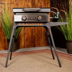 an outdoor bbq grill sitting on top of a wooden table next to potted plants