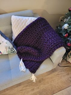 a purple crocheted blanket sitting on top of a couch next to a christmas tree