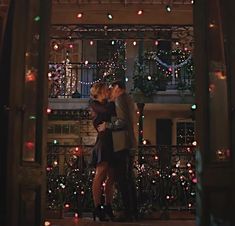 two people standing in front of a building with christmas lights on the windows and balconies