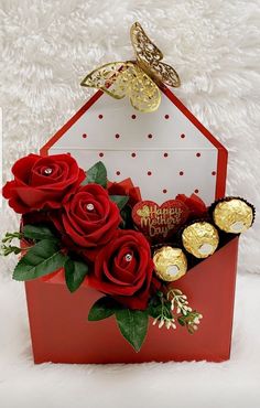 a red box filled with chocolates and roses on top of a white furnishing