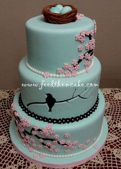 a three tiered blue cake with birds nest on top and pearls around the edges