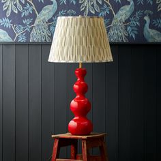 a red table lamp sitting on top of a wooden stool next to a blue wall