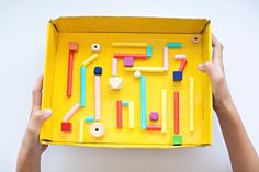 two hands holding up a yellow box with different colored sticks and magnets on it