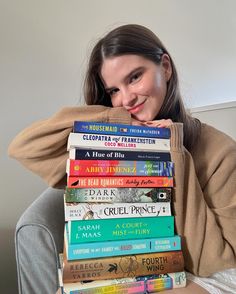 a woman sitting on a couch holding a stack of books