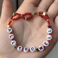 a hand holding a red beaded bracelet with white letters and gold stars on it