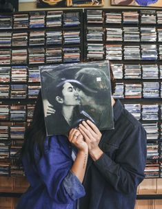 a woman covering her face with a vinyl album in front of a wall of cds