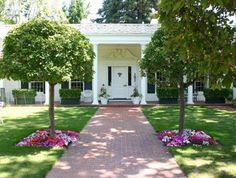 a white house with trees and flowers in the front yard