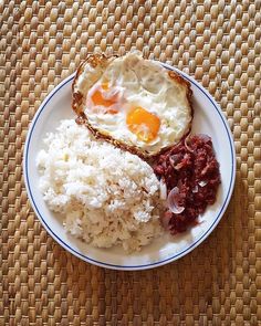 rice, meat and eggs are on a plate with an egg in the middle next to it