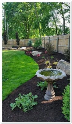 a bird bath sitting in the middle of a lush green yard next to a wooden fence