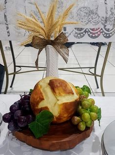 bread and grapes on a wooden platter in front of a white tablecloth with an ornate vase