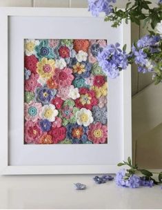 a white frame filled with colorful crochet flowers next to purple and blue flowers