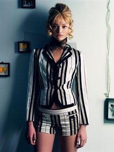 a woman is standing in front of a wall wearing short shorts and a striped shirt