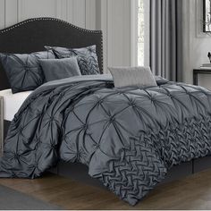 a bed with grey comforter and pillows in a room