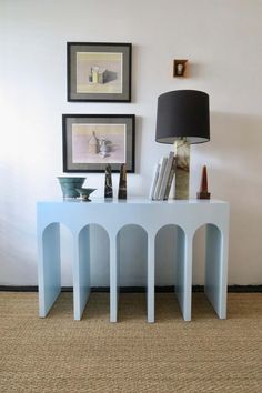 a white table sitting in front of a wall with pictures on it and a lamp next to it