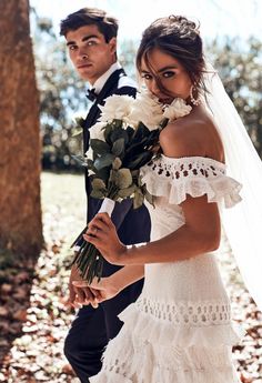 the bride and groom are walking through the woods with flowers in their hand, holding each other's hands