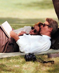 a man and woman laying on the ground kissing under a tree with an open book