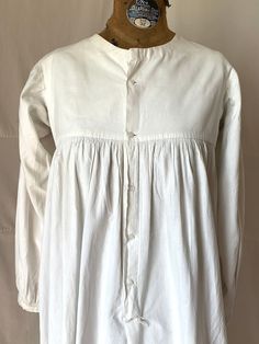 "1815. 32\" bust, white cotton chemise  with long wide sleeves, round neckline, bounle lined yoke, high waisted bodice. Chemise has full skirt to floor and fastens in front, from neck to below knees  with 5 small white glass buttons. Measurements: 32\" bust  Shoulder to shoulder 14\" Shoulder to hem  46\" Ar.holes 7\" Sleeves 20\" Neckline 7\" wide, 3\" deep  Width at bottom 72\" Condition very good,  small rust dots in front" Classic Cotton Prairie Dress For Daywear, White Cotton Peasant Prairie Dress, Historical Design Long Sleeve Dress For Daywear, Historical Long Sleeve Dresses For Daywear, Victorian Long Sleeve Dress For Daywear, Long Sleeve Dresses With Historical Design For Daywear, Cotton Blouse With Covered Buttons For Daywear, Cotton Victorian Dress With Buttons For Daywear, Victorian Prairie Dress With Long Sleeves For Daywear