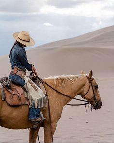 a man in cowboy attire riding a horse through the desert with sand dunes behind him