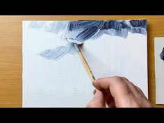 someone is painting something with blue and white colors on the paper, next to another piece of art