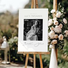 an easel with a photo on it next to a flower arrangement and a sign that says, welcome to lily thomas