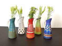 four colorful vases with plants in them on a table