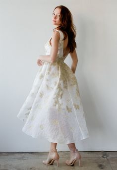 a woman in a white and gold dress is standing against a wall with her back to the camera