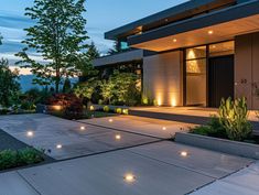 a modern house lit up at night with lights on the front porch and landscaping around it