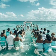 a group of people sitting in the ocean on their wedding day, all dressed in blue and white