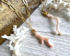 two necklaces with coral and gold chains on a wooden table next to a book