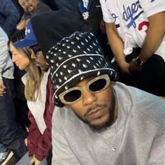 a man wearing sunglasses and a hat sitting in the stands with other people behind him