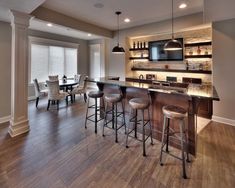 an open concept kitchen and dining room with wood flooring, stainless steel appliances and bar stools