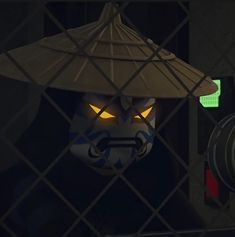 a mask with glowing yellow eyes behind a chain link fence in a dimly lit room