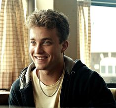 a young man sitting in front of a window smiling