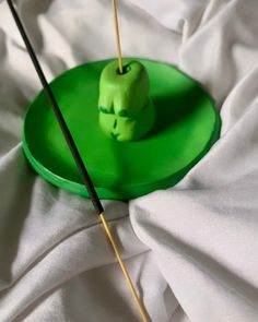 an apple on a green plate with two black sticks sticking out of it and some white sheets in the background