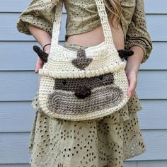 a woman holding a crocheted purse with a monkey face on the front and side