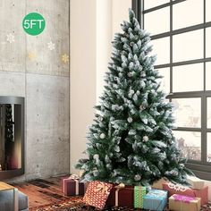 a christmas tree with presents under it in front of a fire place and window sill