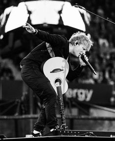 a man holding a guitar while standing on top of a stage in front of a microphone