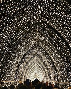 people are walking through a tunnel covered in lights