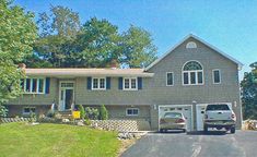 two cars are parked in front of a large gray house with white shuttered windows