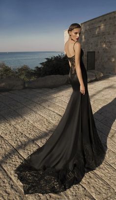 a woman in a long black dress standing on the beach