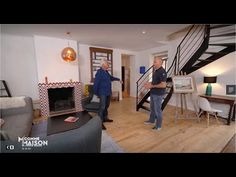 two men standing in a living room talking to each other with a spiral stair case behind them